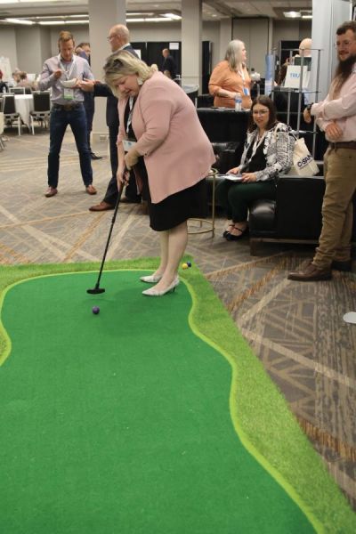 NNA Director Peggy Scott, assistant publisher, Leader Publications, Festus Missouri, putts at the Interlink booth in the NNA Trade Show. Note the newsprint design on Scott s heels!